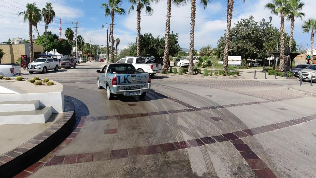 Dash cam view entering a palm-lined roundabout behind a white pickup.