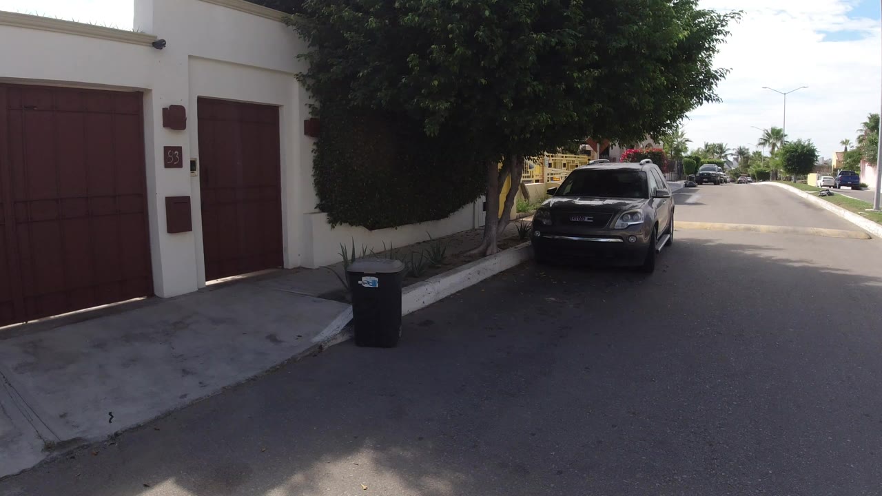 Residential street with red garage doors, trees, trash bin, and parked SUV.