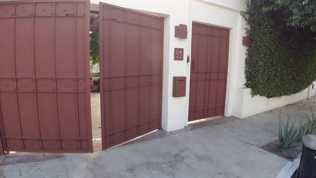 Red metal gate partly open beside a white stucco home entrance.