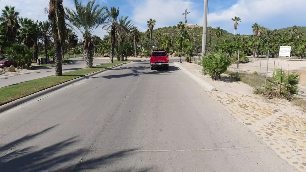 Red pickup passes a fenced sandy area and roadside sign.