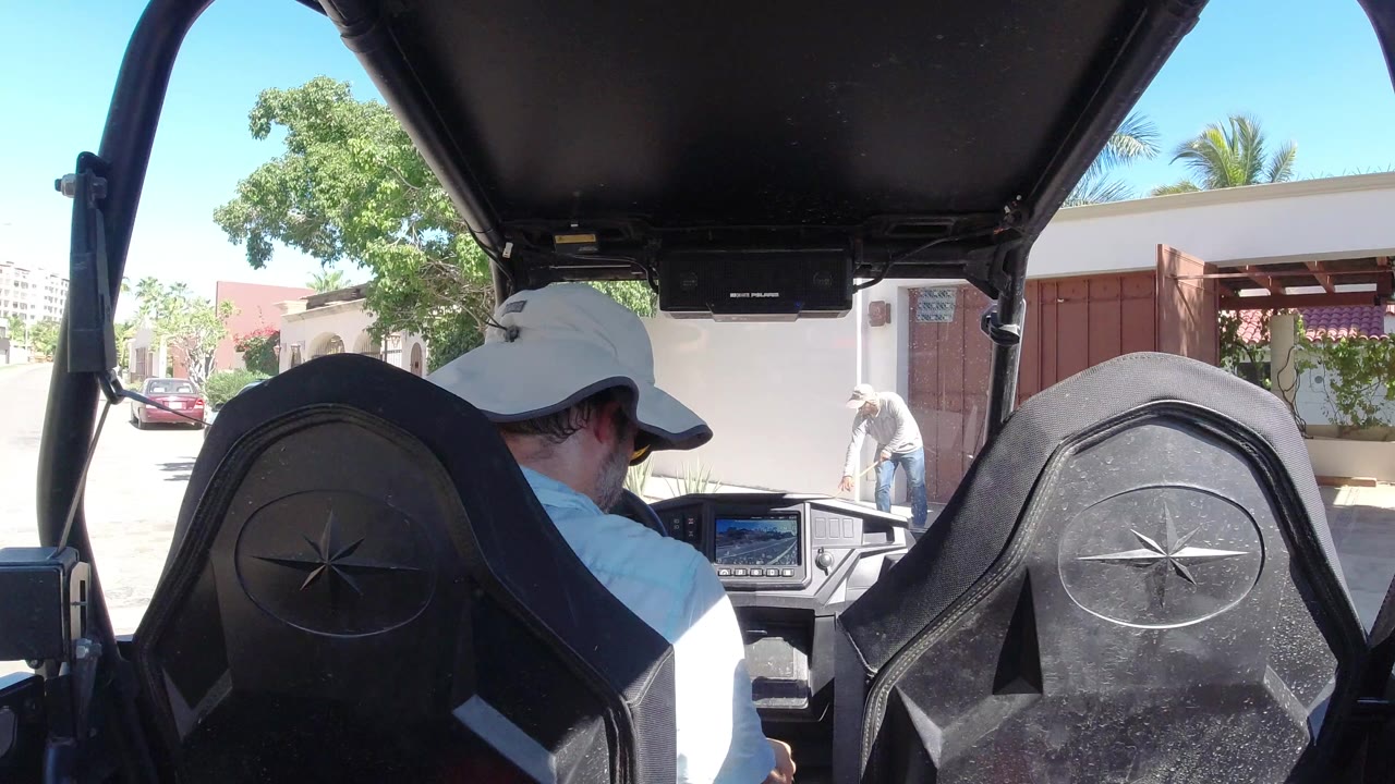 Back-seat view of a man in a white hat inside an open off-road vehicle.