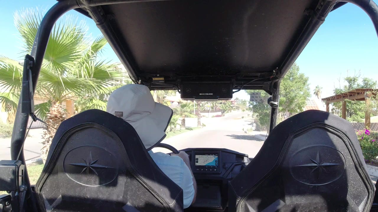 One second in, the Los Cabos street remains centered between the black seats, with the white-hatted driver, palm fronds, and planted roadside areas visible.