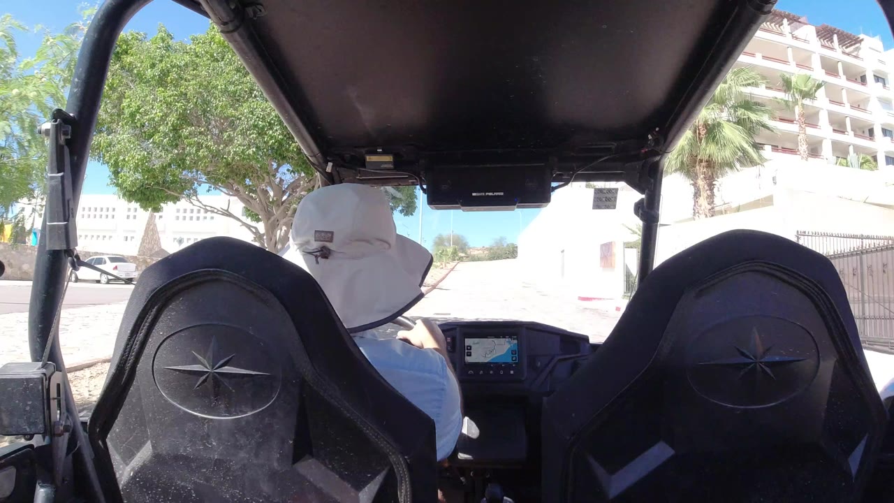 Rear-seat view inside an open off-road vehicle with a driver in a white sun hat.