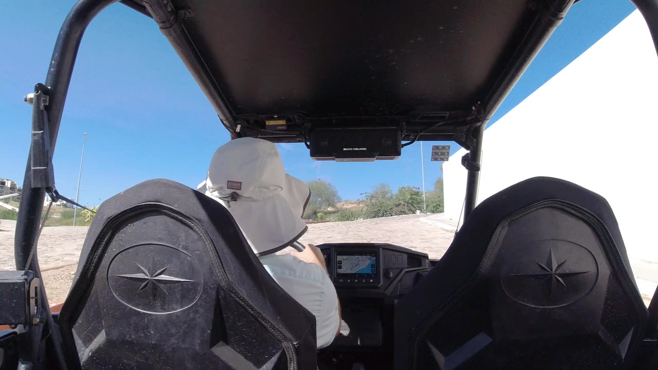 Rear passenger view inside an open vehicle behind a driver in a white hat.