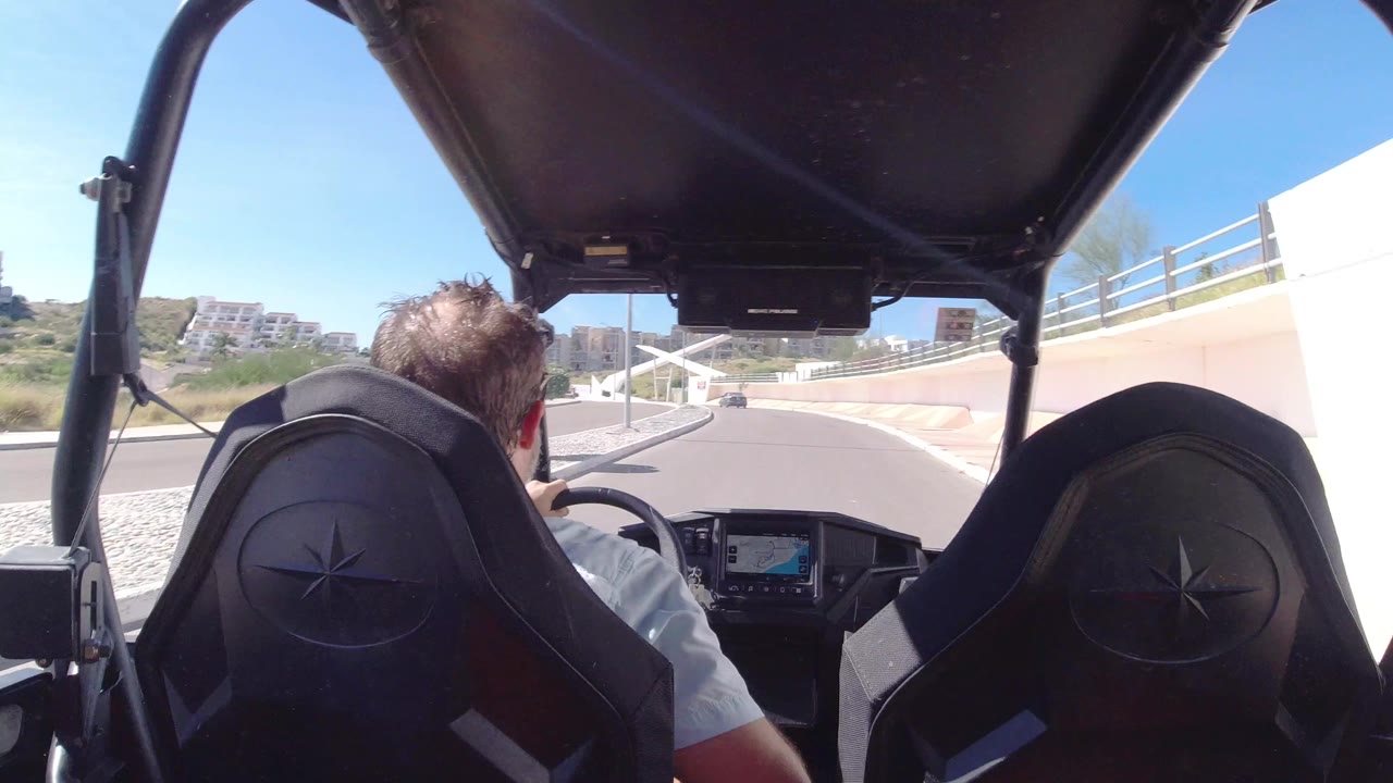 Rear passenger view of a man driving a golf cart on a sunny road.