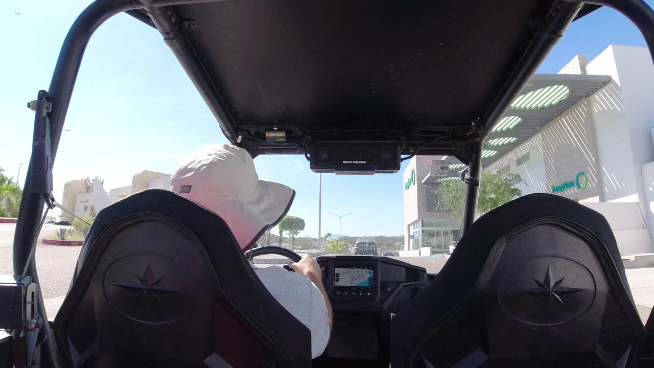 Driver seen from behind inside an open vehicle on a sunny city street.