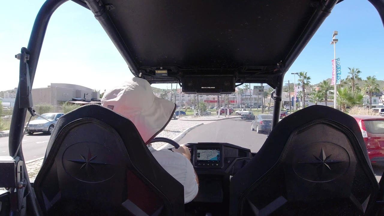 Rear-seat view of a driver in a white sun hat on a sunny road.
