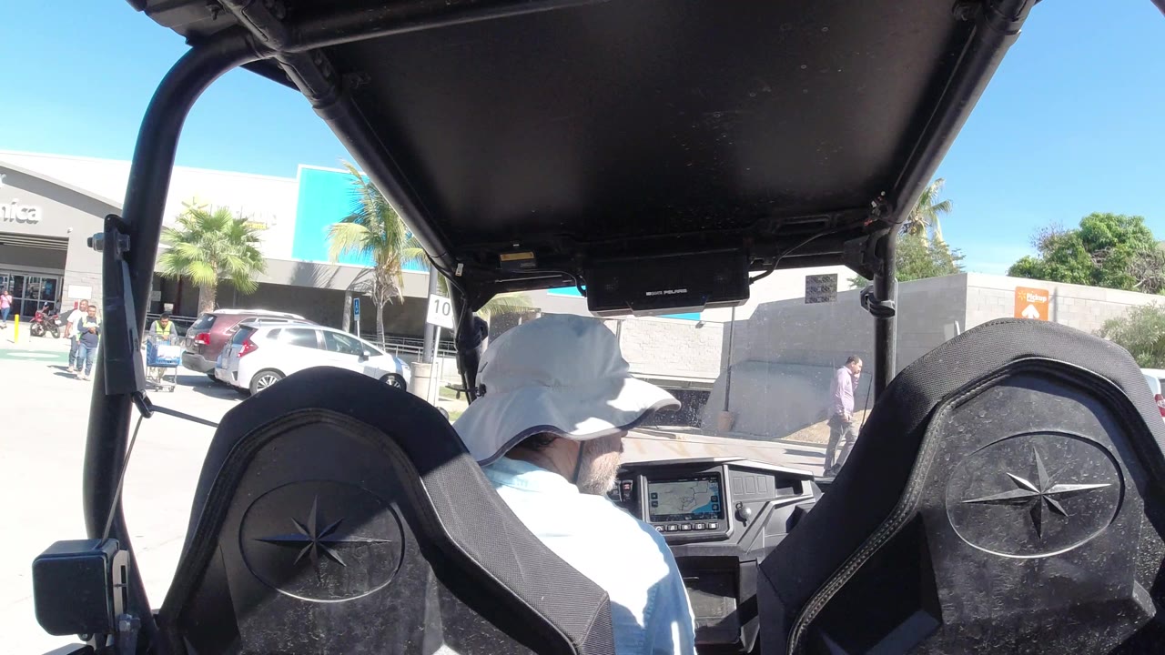 One second in, the hat-wearing driver remains centered under the vehicle roof while the Walmart storefront, parked cars, and small pedestrians stay visible ahead in Los Cabos, Mexico.