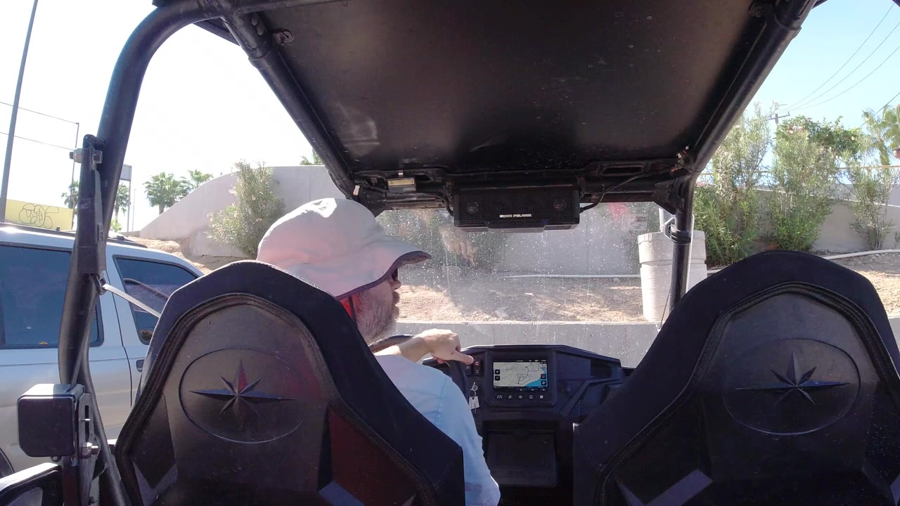 Man in a white hat driving an open vehicle in bright sun.