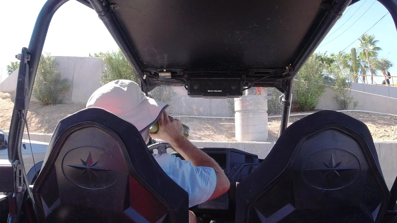 Man in a white hat sits inside an open vehicle holding a cup.
