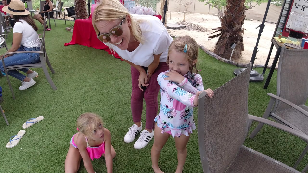 Woman leaning near two young girls beside patio chairs on artificial turf.