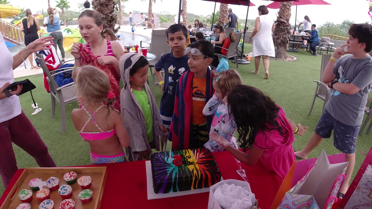 Children and adults gathered beside cupcakes at a poolside club table.