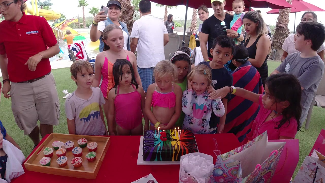 Children and adults gathered around a birthday table outdoors.