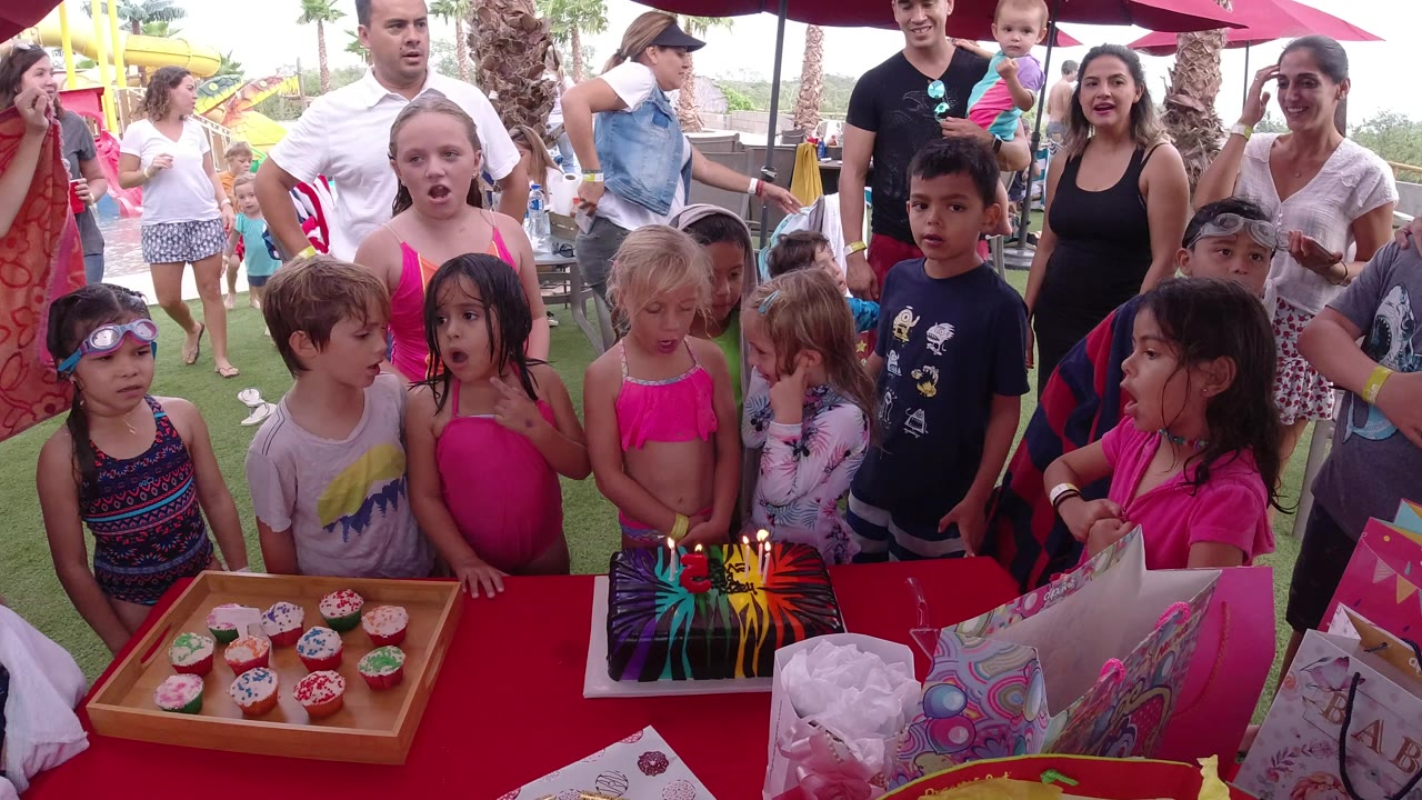 Children and adults gathered around a birthday table with cake and cupcakes.