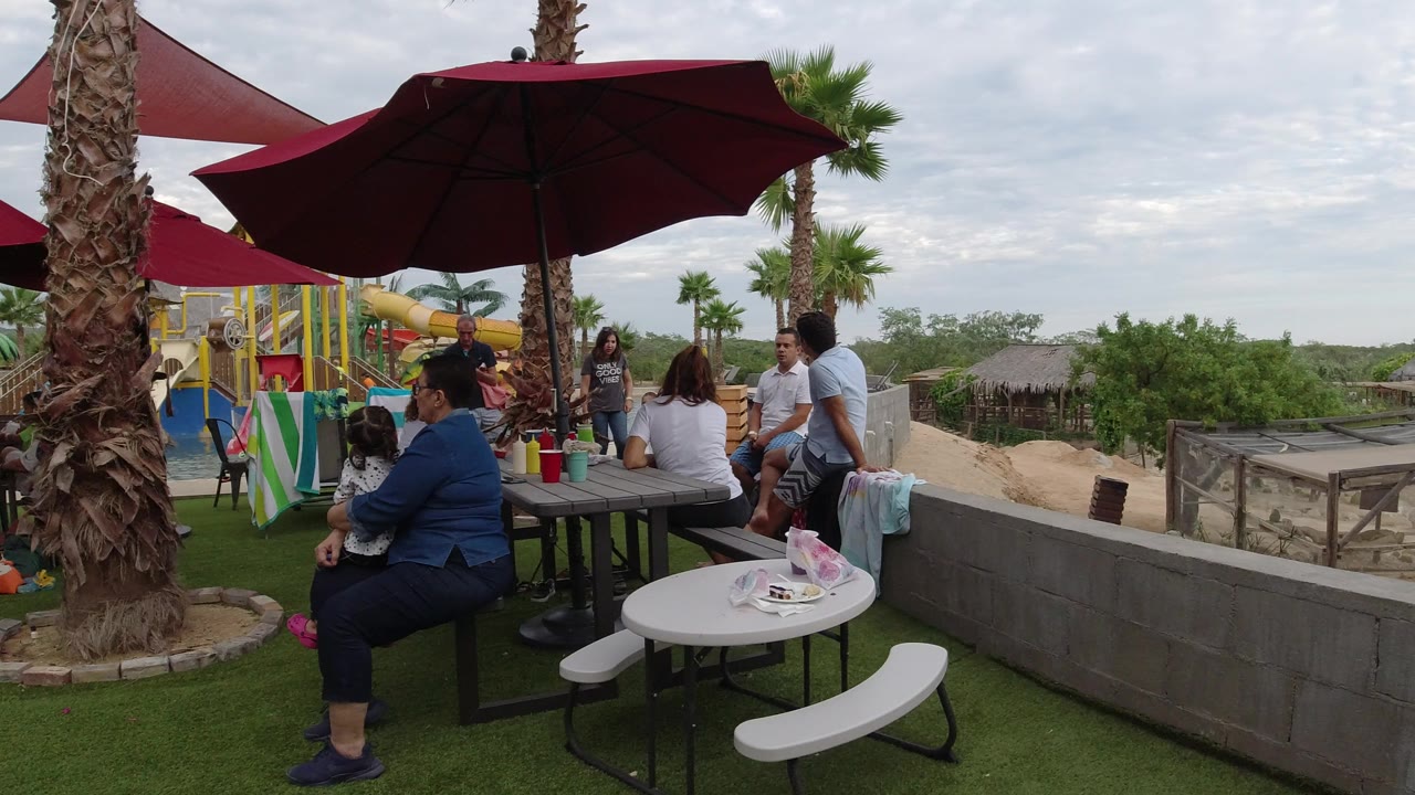 People gathered at outdoor tables under burgundy umbrellas beside a play area.
