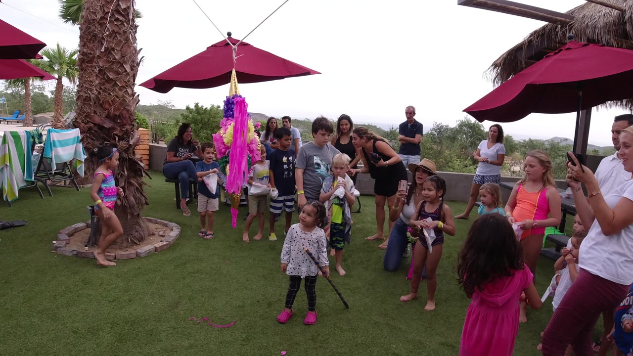 A young child stands in front of the hanging pinata as other children and adults watch from the lawn and patio seating area in Los Cabos.