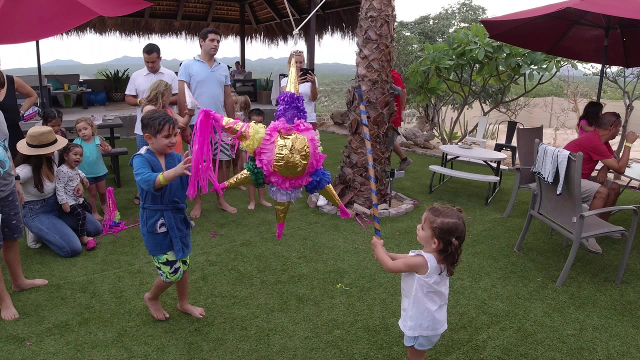 Children gather near a colorful pinata as adults watch on an outdoor patio.
