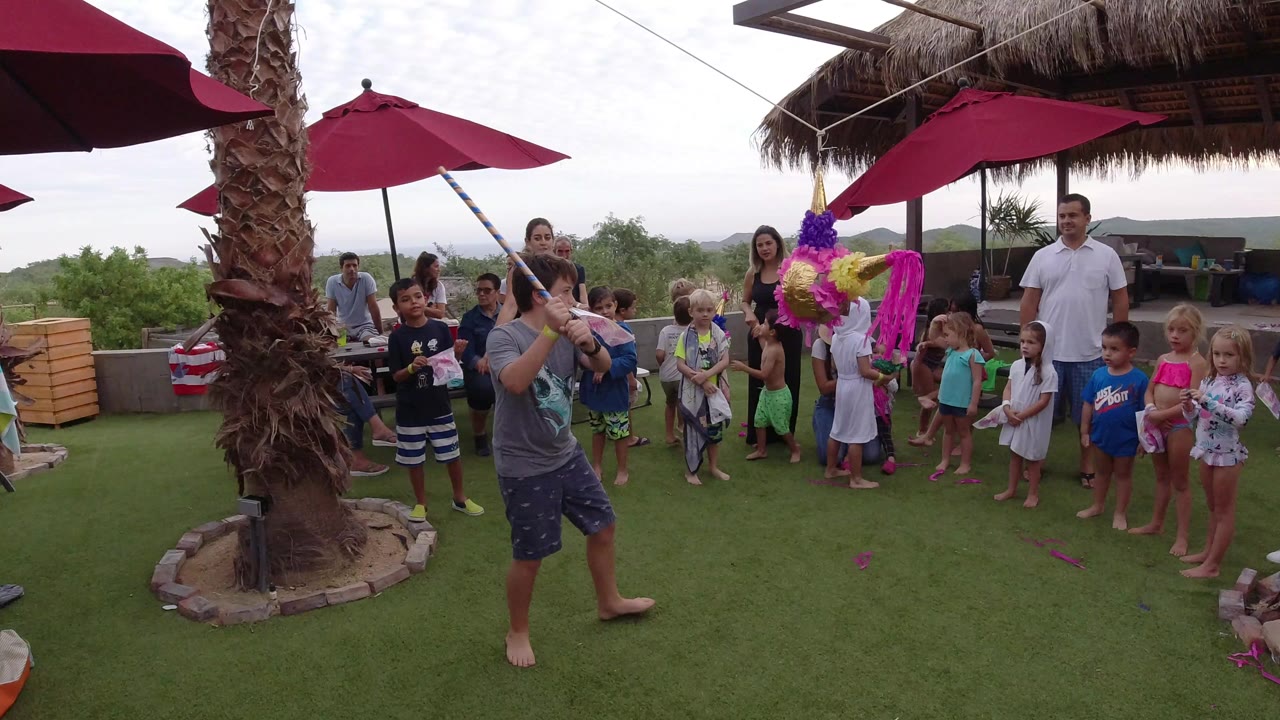 Young man swings at a colorful pinata while children and adults watch outdoors.
