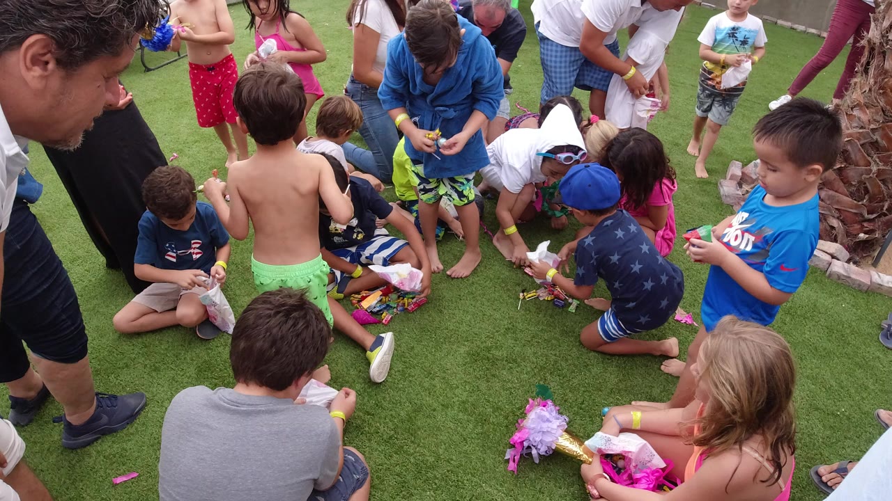 Children and adults gather around a game on grass.