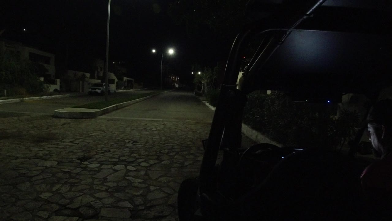 A low-light Los Cabos street view holds on the parked Wrangler edge in the foreground, with streetlights and homes lining the background and no visible people.