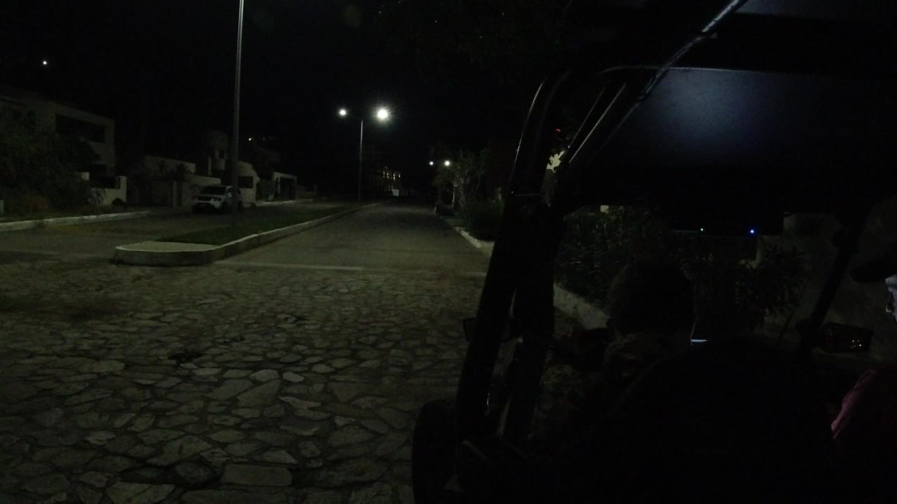 A similar Los Cabos street angle shows the vehicle roof and frame in deep shadow, with two silhouetted people facing the lit cobblestone roadway and houses.