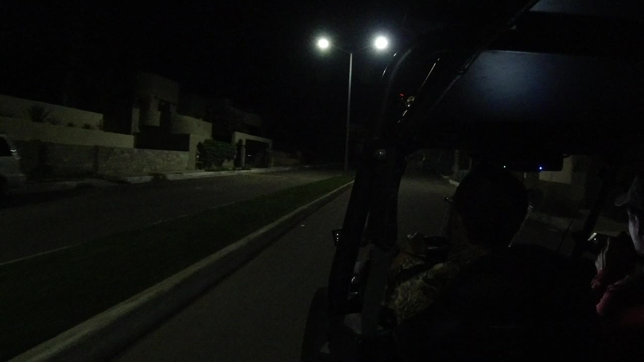 Night road seen from an open vehicle with passenger silhouettes.