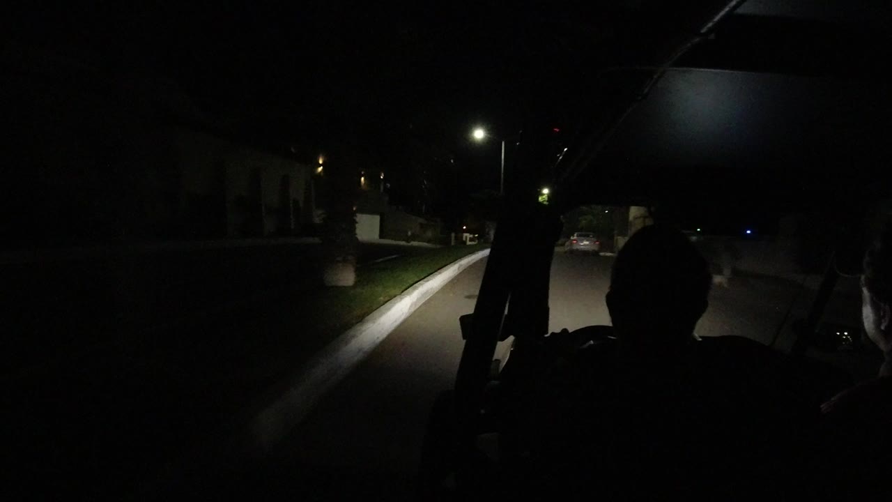 Night road seen from inside an open vehicle with a passenger silhouette.