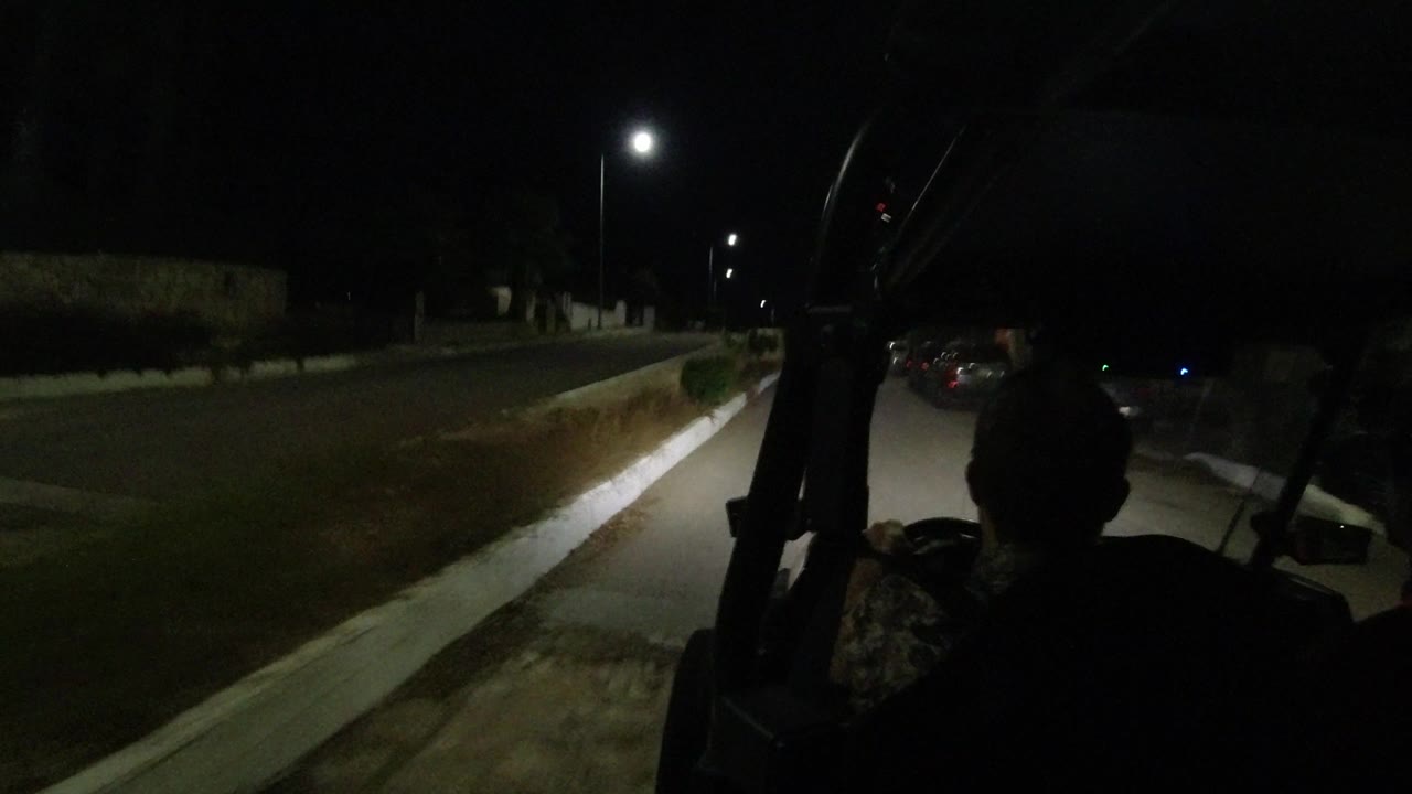 The Los Cabos night drive continues with the rider silhouette centered low in frame, a bright streetlamp overhead, and the curb guiding the road edge.