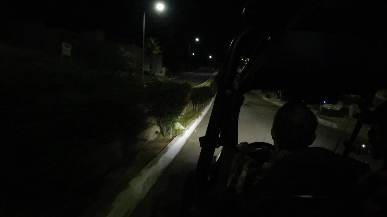 Inside a golf cart in Los Cabos at night, silhouetted passengers face a dim residential street lit by a bright overhead streetlight.