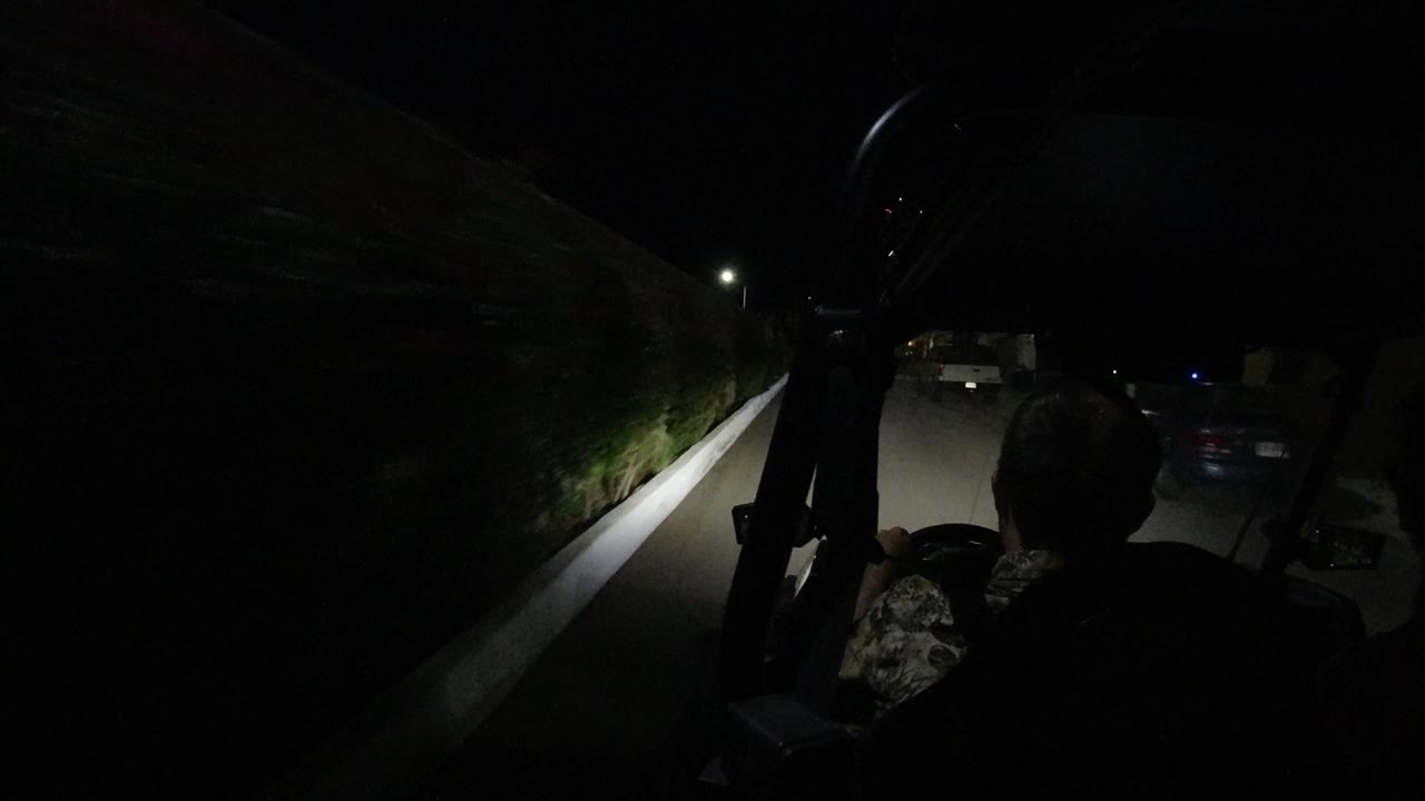 A silhouetted driver is seen from behind in the RZR as the road runs beside a high stone wall and a parked car in Los Cabos, Mexico.