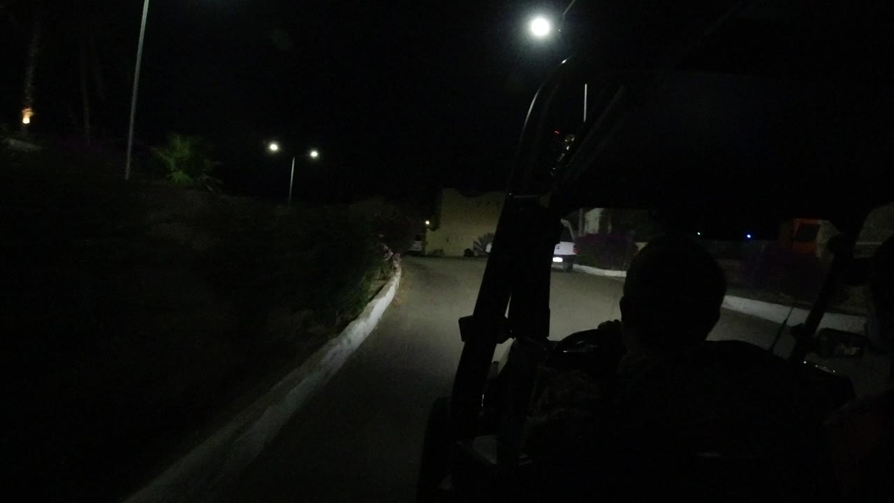 Silhouetted golf cart driver on a dark road under streetlights.