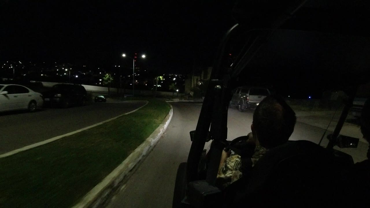 Silhouetted driver on a dark curving road with parked cars and streetlights.