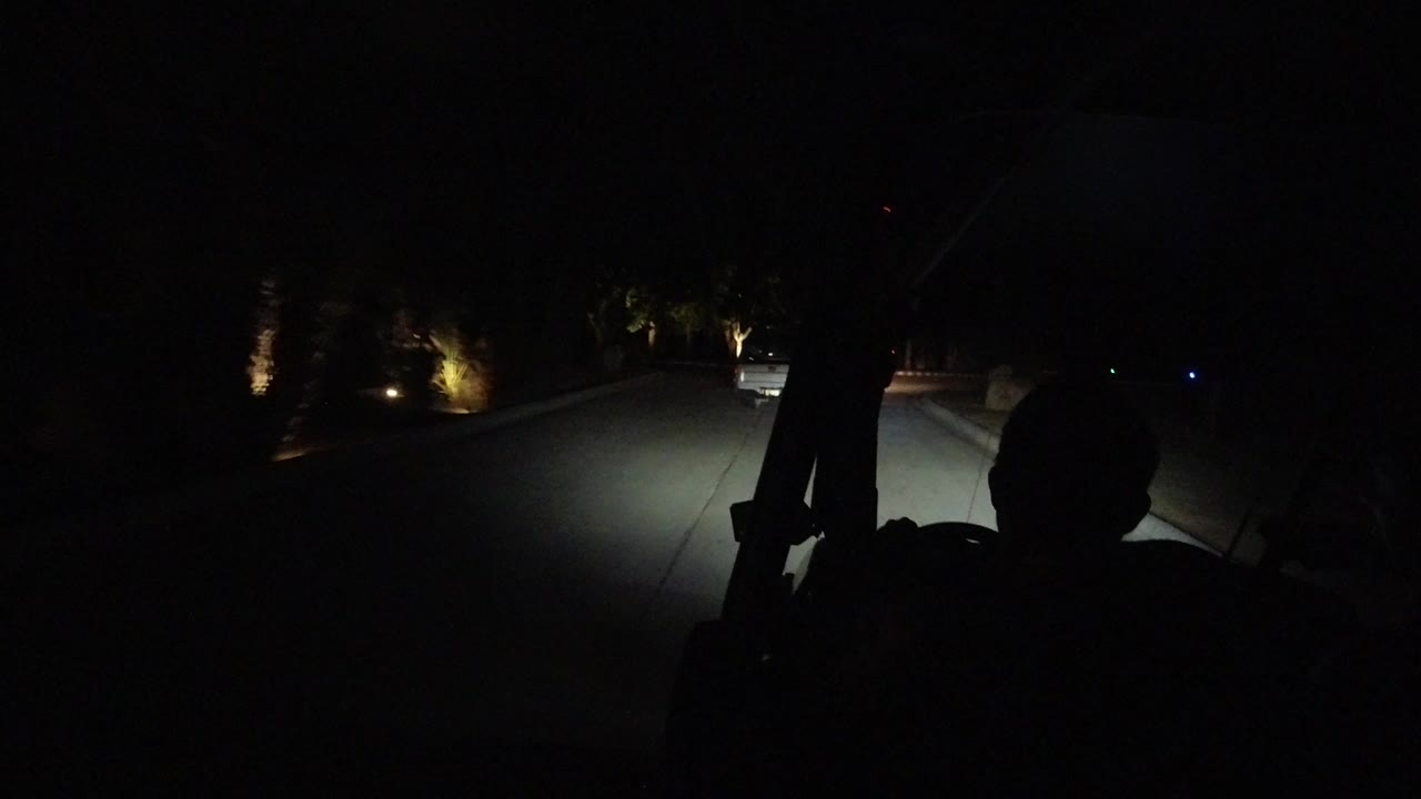 Nighttime road view in Los Cabos, Mexico, seen through a dark vehicle windshield with headlight spill on the lane and roadside lamps ahead, with no clear visible people.