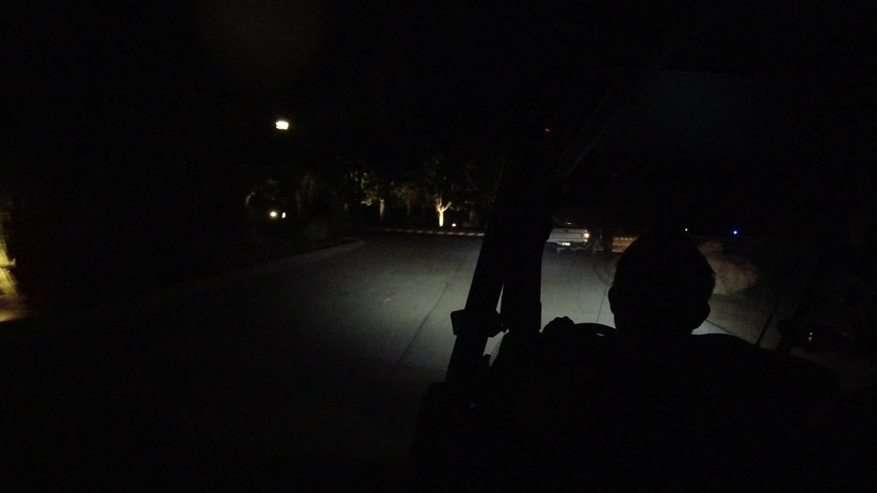 Dark vehicle interior frames a night road with a car shape near the right edge.