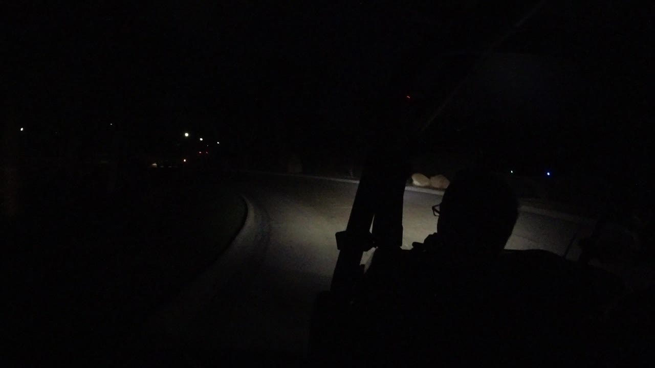 Dark road ahead lit by headlights with deep foreground shadows.