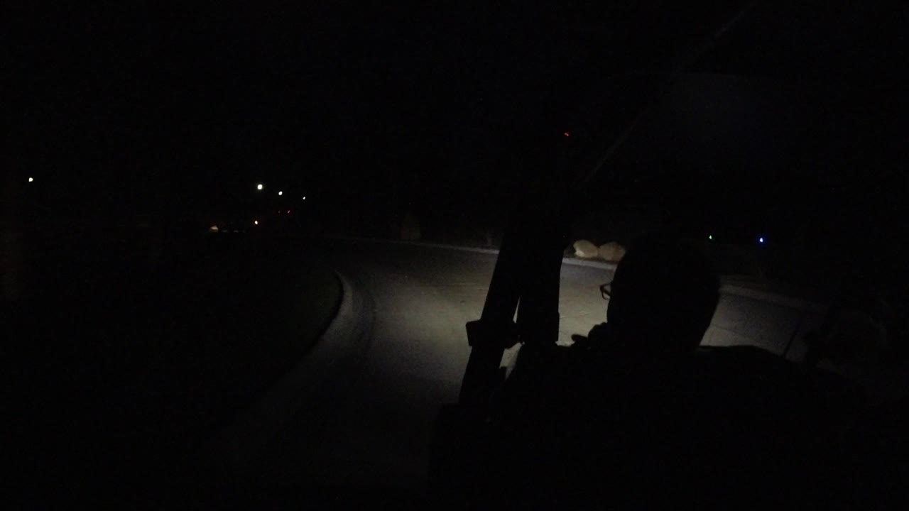 The Los Cabos Mexico road remains mostly black, with a headlight patch on the pavement and a few distant lights marking the background.
