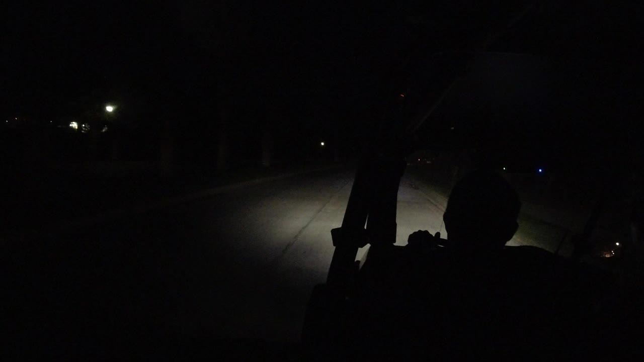 Dark car interior with driver silhouette and headlights on a road.
