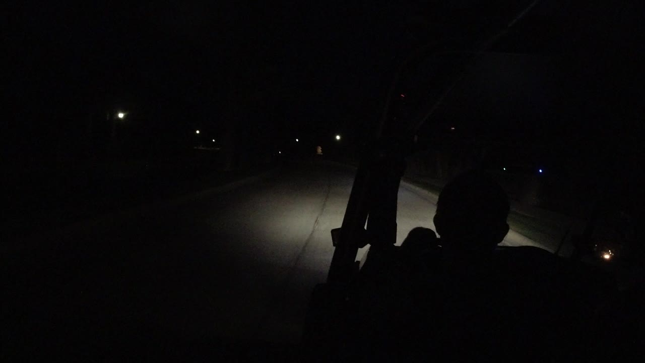 Dark road ahead lit by vehicle headlights at night.