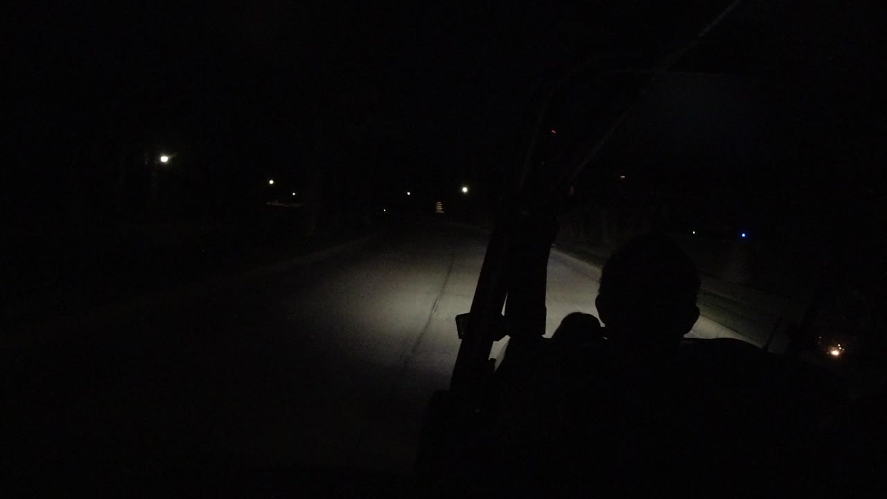The road continues through darkness in Los Cabos, with scattered streetlights ahead and a black foreground silhouette inside the vehicle.