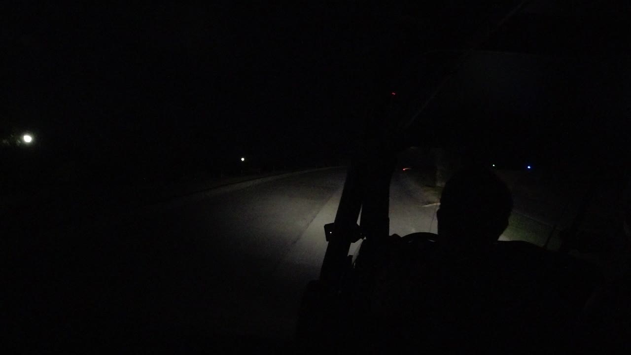 A dark Los Cabos, Mexico road frame shows the lit pavement bending ahead, small distant lights, and no visible people.