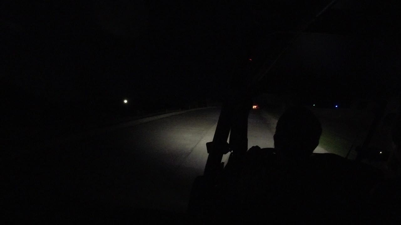 The highway remains mostly black in this Los Cabos, Mexico frame, with a bright patch of headlights on pavement and no visible people.