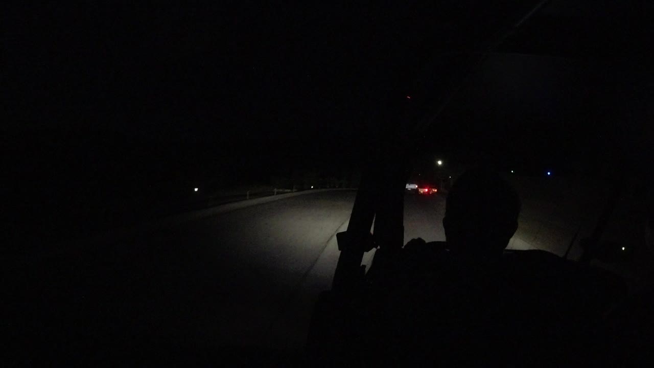 Dark road seen past a silhouetted passenger inside a vehicle.