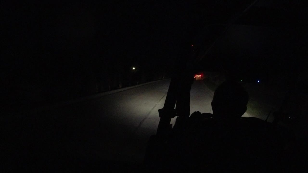 Dark over-the-shoulder road view from a vehicle at night.