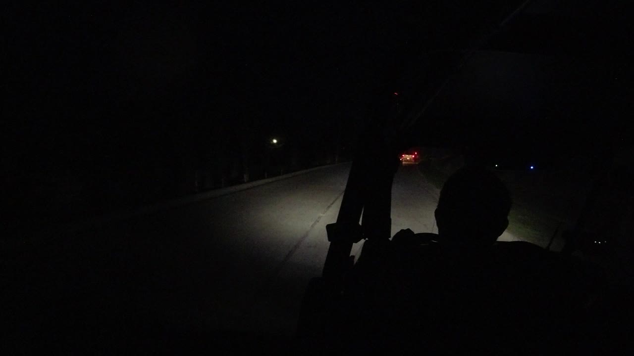 A silhouetted rider remains centered in the foreground while the road curves into darkness and the headlights illuminate the pavement in Los Cabos, Mexico.