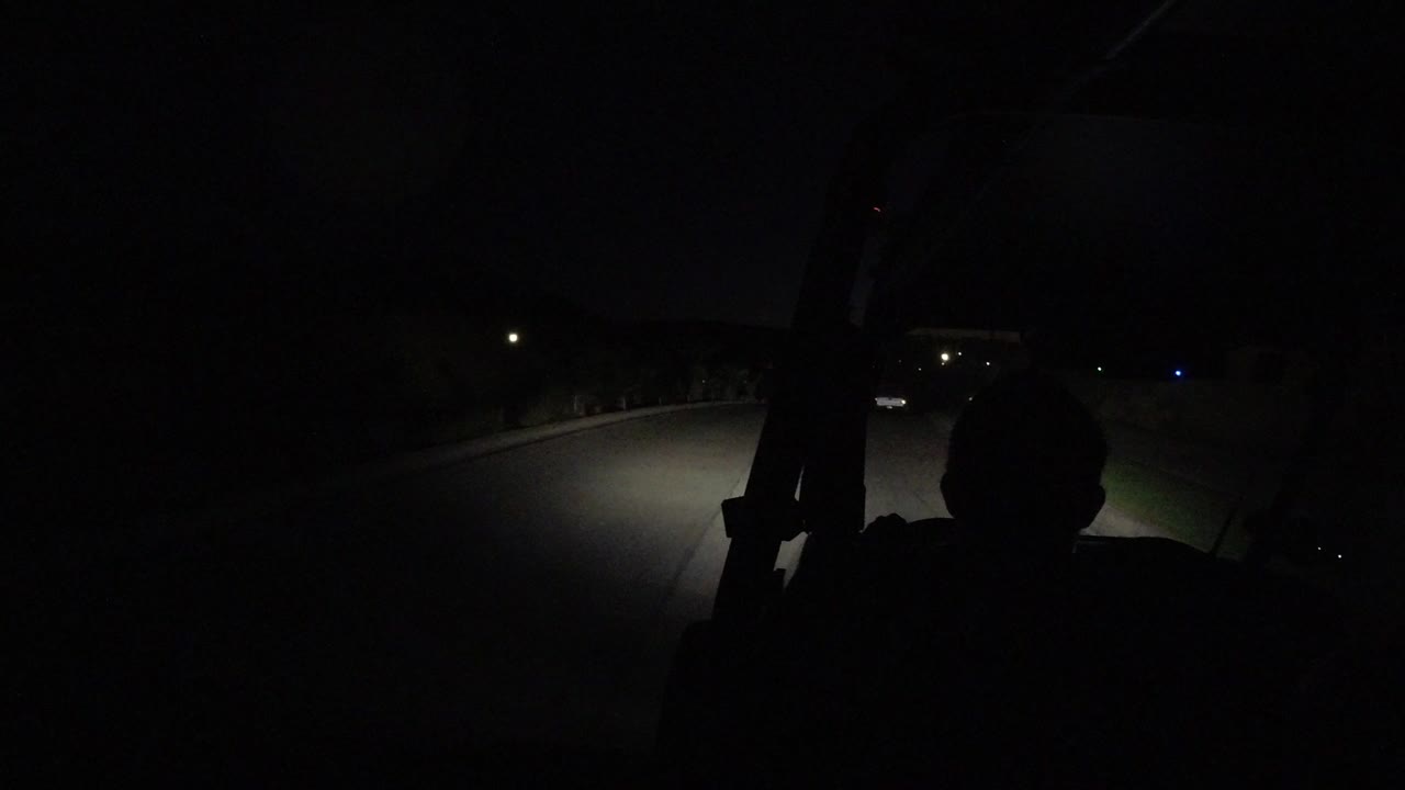 Dark golf cart interior with headlights lighting a road ahead.
