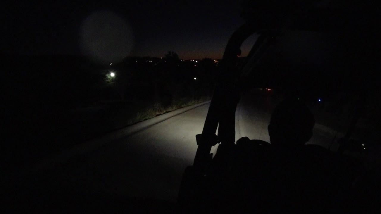 Dark road lit by vehicle headlights with a silhouetted person in the foreground.