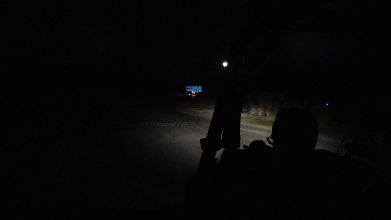 Los Cabos night driving frame with the vehicle interior in silhouette, a bright headlight cone on the road, and no recognizable people or faces.