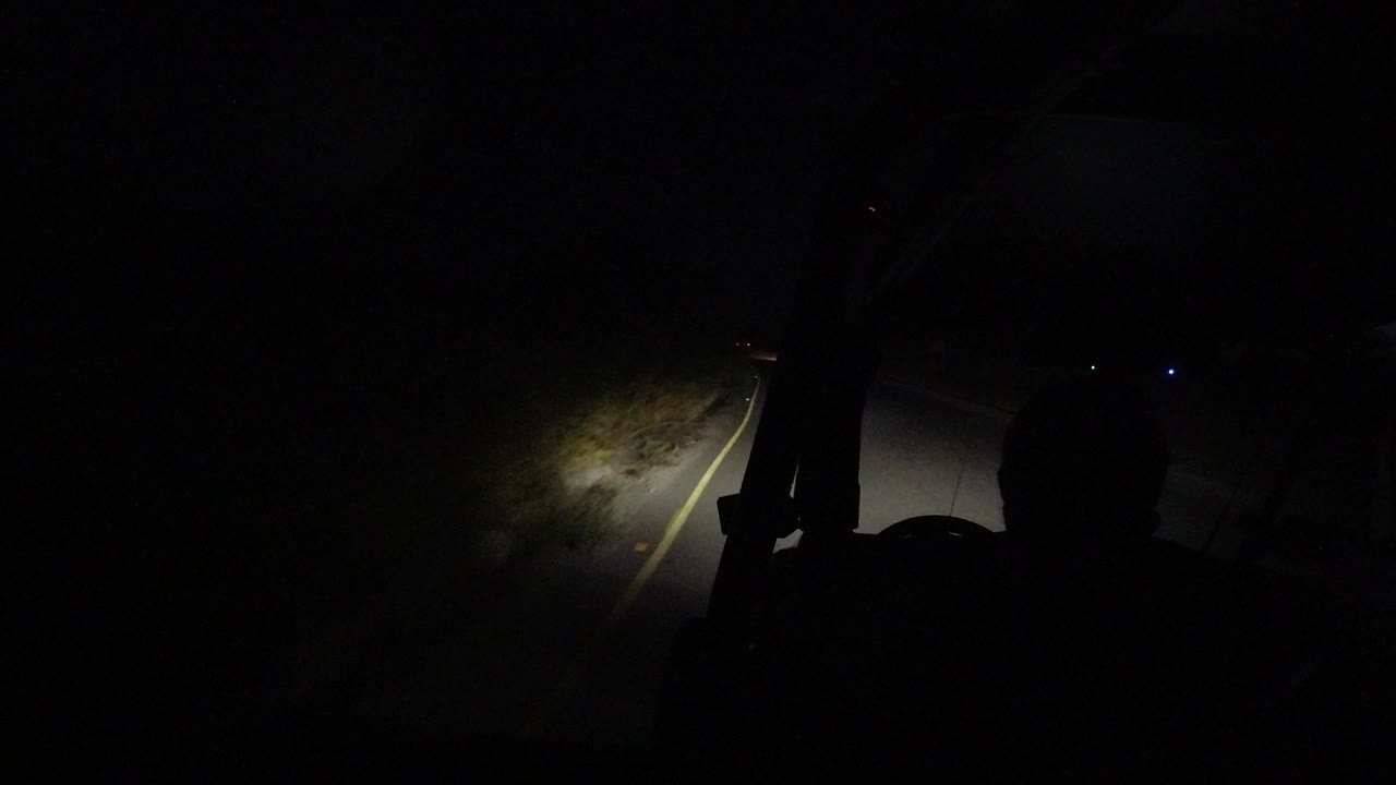 Dark cabin silhouette frames a headlit road edge.