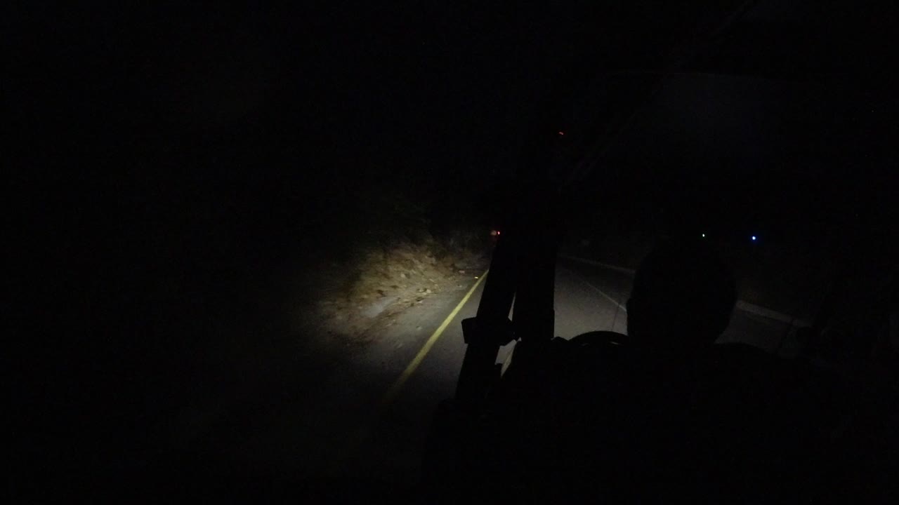Dark road ahead lit by a small beam from a jeep.