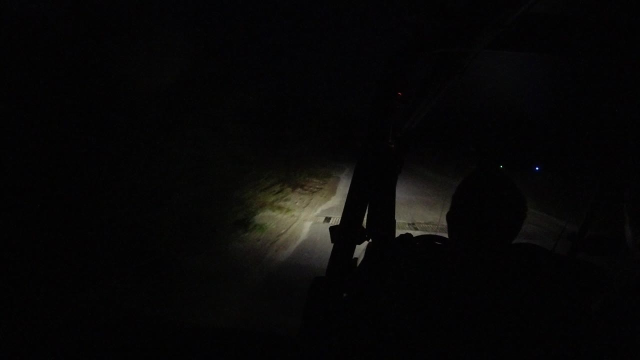 At 0:01 in Los Cabos, Mexico, the headlight beam shifts across pale sand and the road edge while the rest of the scene remains almost black, with no clearly visible people.